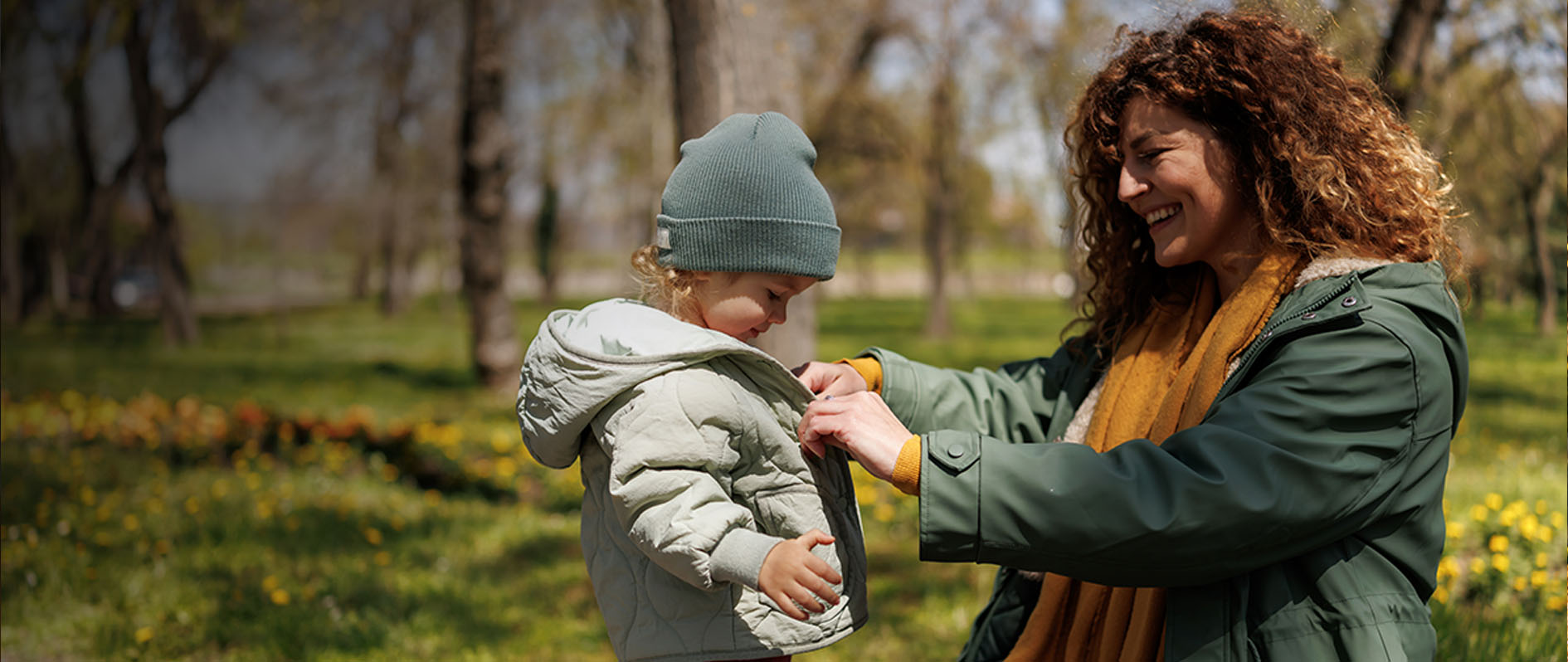 Caring mother buttoning her daughter's jacket during cold early spring day in the park 